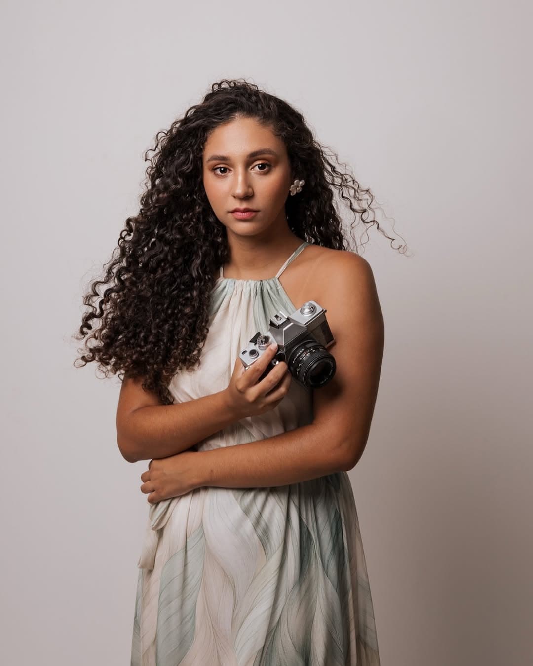 Gabriela Castro com um vestido claro segurando uma câmera fotográfica